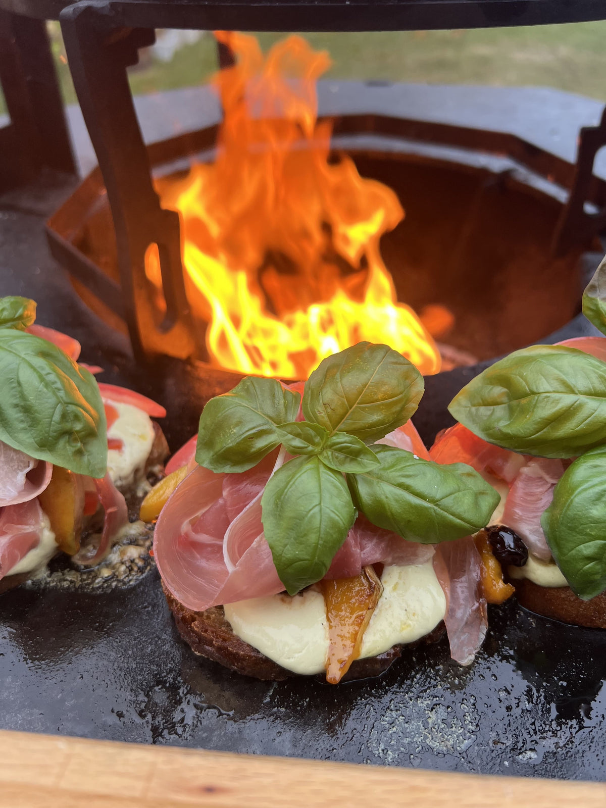 Burger mit Schinken, Mozzarella und Basilikum vor offener Flamme